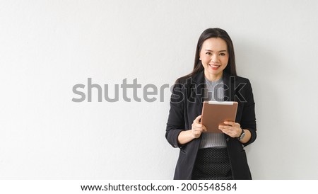 Portrait of a cheerful confident Asian businesswoman in a business suit holding and using a digital tablet in the business building. Business stock photo
