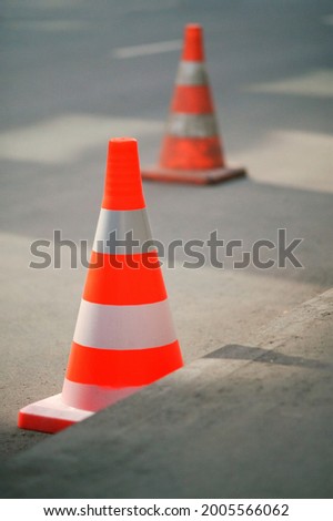 Two safety cones on asphalt road. New cone on front in focus, old on background blurred.