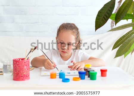 A little talented girl makes sketches of a drawing with a pencil, then to paint it with paints from cans. Creative development of preschool children. Selective focus on the face