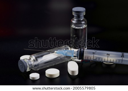 Vial Drug Vaccine Plastic Syringe with Needle and medicine tablets on black background. Close-up, selective focus.