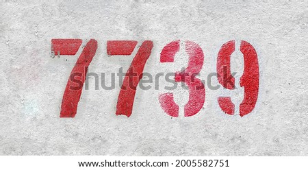 Red Number 7739 on the white wall. Spray paint. Number seven thousand seven hundred thirty nine.