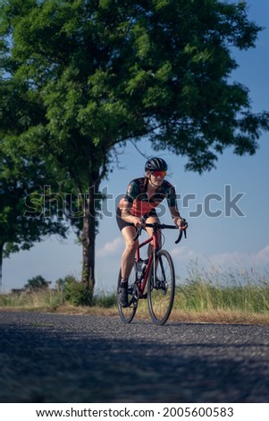 Vertical, Angle photo of a young woman, pedaling, riding speed a road bike, on a ride through nature. Gender equality in sport Concept. Royalty-Free Stock Photo #2005600583