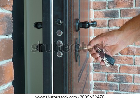 The man inserts the key into the lock to close the armored door of the house.                                Royalty-Free Stock Photo #2005632470