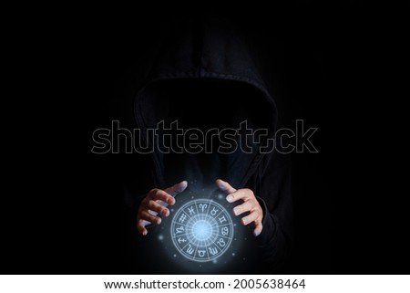 Young woman's face is not visible in a black hood holding with palms a glowing zodiac circle on a black background.