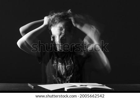 portrait frustrated schoolboy with long exposure dark room with blurred movement and effect ghost screams doing homework. concept learning difficulties, home schooling, childhood