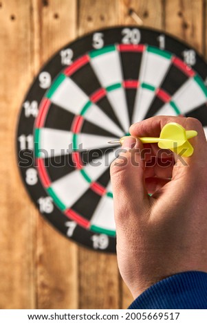 Darts game. Throwing darts at the target. The player holds a yellow dart in his hand on the background of the dart board Royalty-Free Stock Photo #2005669517