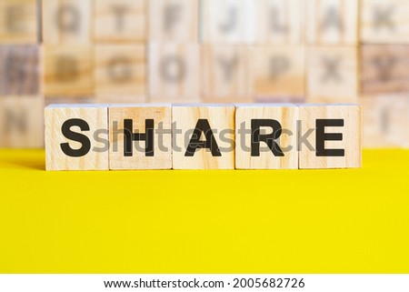 the word share is written on wooden cubes on a bright yellow surface. in the background are rows of cubes with different letters. business and finance concept