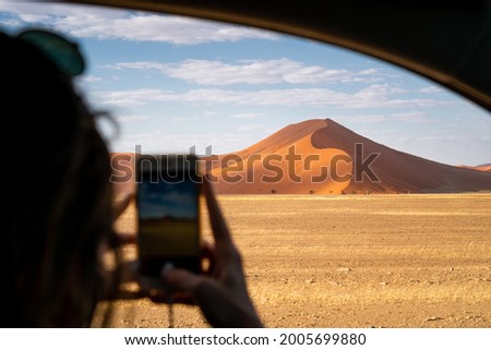 Tourist taking cell phone photo of giant sand dune at sunrise near Sossusvlei in the Namib-Naukluft National Park, Namibia, Africa.