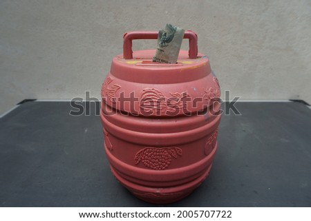 Picture of red cylinder shaped piggy bank   and money inserted on its hole.