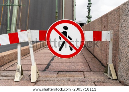 Barrier blocking sidewalk and sign with picture of crossed-out man prohibiting the passage of pedestrians, because the area is under repair or it is dangerous, front view.