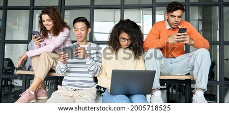 Young diverse multiracial cool group of high school college students girls and guys sitting at university campus space holding technology gadgets using digital devices studying together. Royalty-Free Stock Photo #2005718525