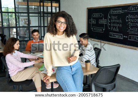 Young happy African American woman team leader sitting on desk holding tablet and international business startup students working studying at desk on project in contemporary classroom office. Portrait Royalty-Free Stock Photo #2005718675