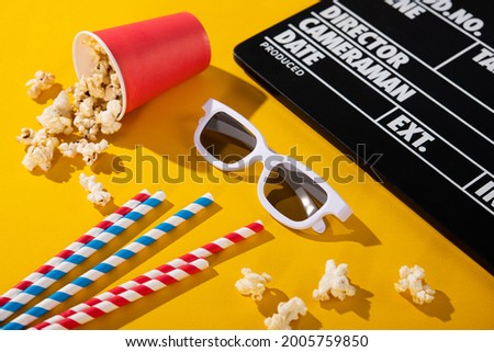 3D glasses, popcorn in a box, clapper board, colored cocktail tube on a yellow background. cinema cocncept.