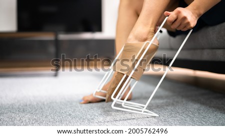 Woman Putting On Medical Compression Stockings Using Stocking Aid Puller Royalty-Free Stock Photo #2005762496