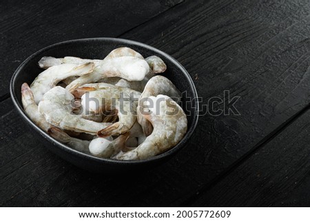 Frozen raw uncooked tiger prawns, shrimps set, on black wooden background, with copy space for text