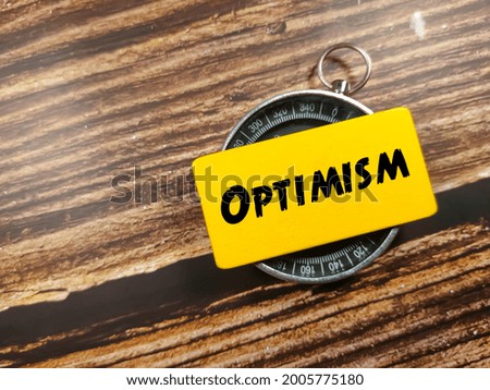 Business concept. Text OPTIMISM on yellow board with compass on wooden table background.