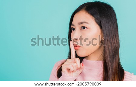 Young Asian beautiful woman with finger in front of mouth on lips, sign of silence gesture saying shh or keeping a secret, studio shot isolated on blue background