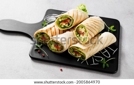 Wrap sandwich, roll with salted salmon fish and fresh vegetables. Light gray background.
