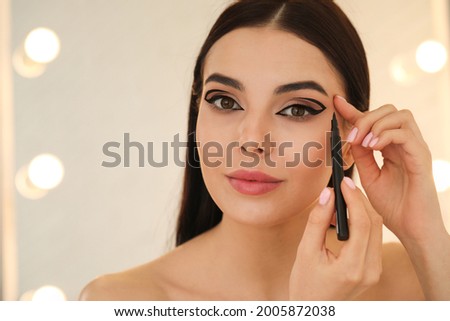 Beautiful young woman applying black eyeliner indoors. Space for text Royalty-Free Stock Photo #2005872038
