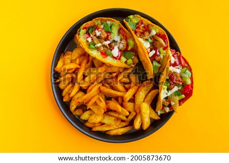 Mexican chicken and vegetables taco with french potatoes in black plate, flat lay on a yellow background, Latin American fast food view from above, close up