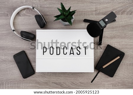 podcast concept - white lightbox with podcast word on the table with microphone, headphones, smartphone and notepad