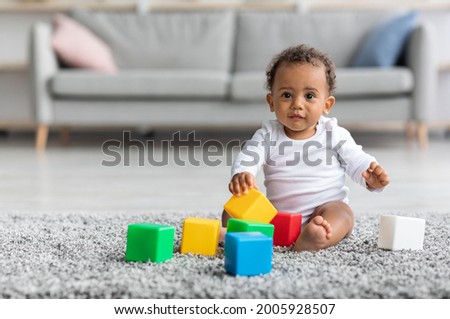 Adorable Black Infant Baby Playing With Stacking Building Blocks At Home While Sitting On Carpet In Living Room, Portrait Of Cute African American Child Using Colorful Constructor Toys, Copy Space Royalty-Free Stock Photo #2005928507