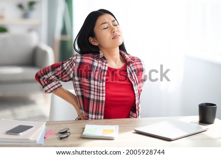 Beautiful Young Asian Woman Suffering From Backache While Sitting At Desk In Home Office, Tired Korean Freelancer Lady Having Acute Lower Back Pain After Long Time Working With Laptop Computer Royalty-Free Stock Photo #2005928744