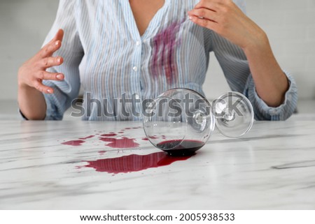 Woman with spilled glass of wine and stain on her shirt at table indoors, closeup Royalty-Free Stock Photo #2005938533