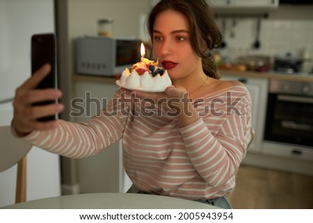 Young birthday girl taking selfie with festive cake. Pretty female holding cupcake with candle. Woman celebrating anniversary with online via videocall with friends. Freelancing and quarantine concept