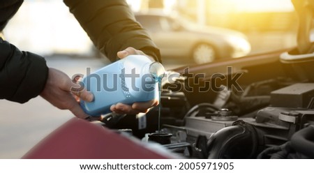 Man filling car radiator with antifreeze outdoors, closeup
