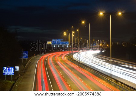 Smart motorway in England, UK with light trails signifying busy traffic at rush hour. The NSL symbols under the gantry sign signify an end to speed restrictions. Royalty-Free Stock Photo #2005974386