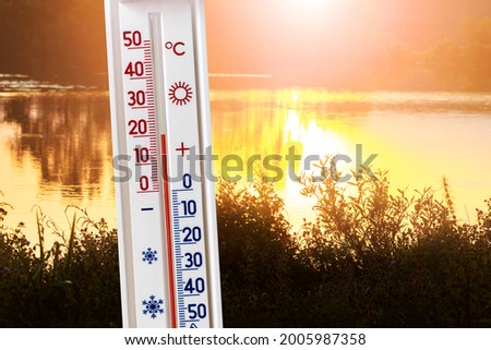 Thermometer on the background of the river at sunset shows 20 degrees of heat. Summer and autumn temperatures in the evening