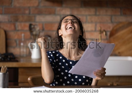 Excited overjoyed young woman getting investment income or good news from financial documents, reading letter, checking papers and making winner yes hand gesture, receiving notice from bank, Royalty-Free Stock Photo #2006035268