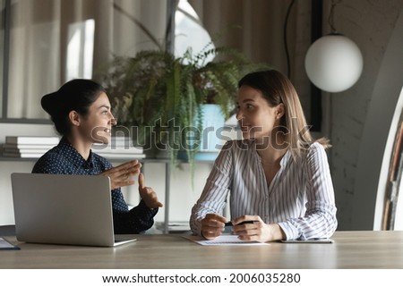Diverse female office employees discussing project, talking at meeting table. Indian mentor explaining work data to intern. Coworkers negotiating on startup, financial report, sharing business ideas Royalty-Free Stock Photo #2006035280