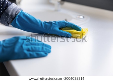 Housewife, cleaner, janitor wearing blue protective rubber gloves, washing table top or kitchen counter white surface with rag. Close up of hands. Household, cleaning service, domestic work concept Royalty-Free Stock Photo #2006035316