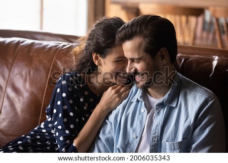 Happy millennial couple enjoying being together in new house, apartment, excited about good news, talking, hugging, laughing, smiling while sitting on luxury leather couch. Love, relationship concept Royalty-Free Stock Photo #2006035343