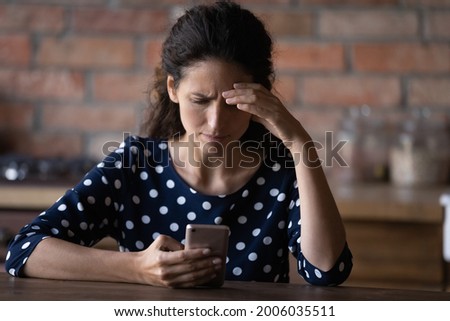 Worried Latin woman having problems with mobile phone, using wrong working apps, getting annoyed with spam, reading message with bad news, feeling stress, angry about cellphone breakdown Royalty-Free Stock Photo #2006035511