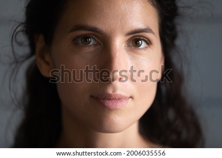 Close up portrait of serious beautiful millennial young woman with smooth healthy skin and black hair looking at camera. Face of Hispanic 30s female model on grey background. Beauty care concept