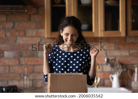 Excited shopper unpacking parcel at home, opening box, making winner joy yes gesture. Happy customer receiving awaited parcel from online shop, getting surprising gift. Delivery service concept Royalty-Free Stock Photo #2006035562