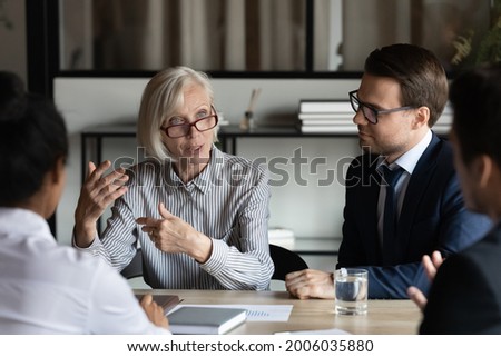 Middle aged mature mentor training interns, corporate coach teaching staff, teacher explaining work process to new employees. Female business leader speaking at meeting, conference, briefing Royalty-Free Stock Photo #2006035880
