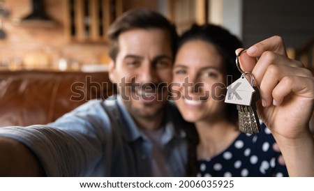 Happy young husband and wife showing key at camera, taking selfie. Property buyers, tenants celebrating mortgage approval, rent apartment, buying first house. New home, real estate concept