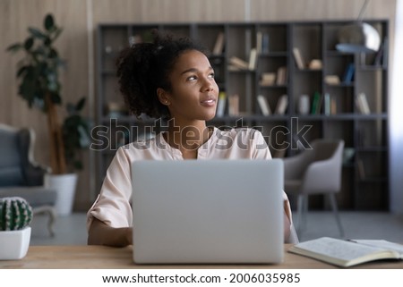 Dreamy African American woman looking to aside, distracted from laptop, sitting at work desk, happy young female dreaming about good future or new opportunities, pondering strategy, planning project Royalty-Free Stock Photo #2006035985
