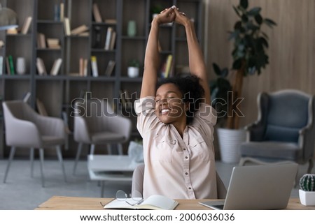 Happy carefree African American woman stretching hands at workplace, leaning back in comfortable chair, student or freelancer relaxing enjoying break after work done, sitting at desk with laptop Royalty-Free Stock Photo #2006036036