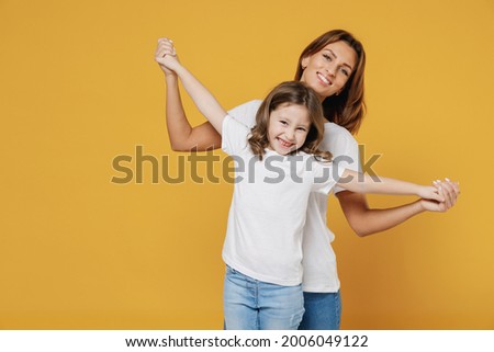 Happy woman in basic white t-shirt have fun dance cute child baby girl 5-6 years old. Mommy mum little kid daughter isolated on yellow orange color background studio. Mother's Day love family concept