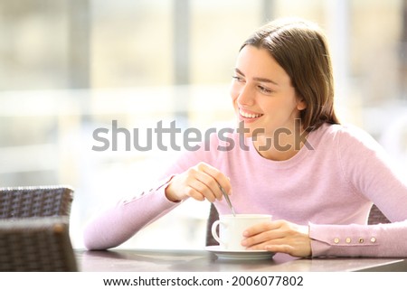 Happy woman stirring coffee sitting in a restaurant terrace