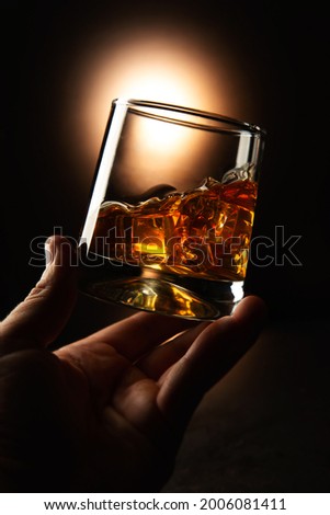 hand holds a glass with whiskey and ice on a dark background. Selective focus Royalty-Free Stock Photo #2006081411