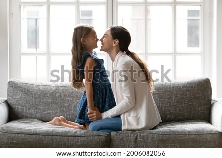 Loving young Caucasian mother and little teen daughter sit relax on sofa in living room play on family weekend. Happy mom and small girl child rest at home feel playful enjoy close moments together. Royalty-Free Stock Photo #2006082056