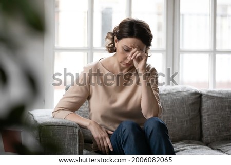 Unhappy old Caucasian woman sit on sofa at home feel lonely distressed lack communication or family support. Upset sad middle-aged female think ponder of health problems. Maturity concept. Royalty-Free Stock Photo #2006082065