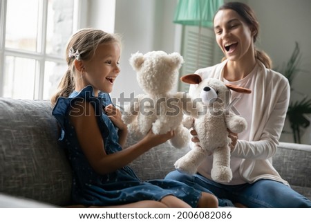 Playful happy young Caucasian mom and small teen daughter have fun play puppet theatre at home. Smiling mother and little girl child engaged in playful game activity with teddy bear toys together.
