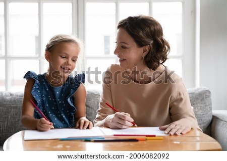 Loving old Caucasian 60s grandmother have fun drawing painting together with small teen granddaughter at home. Caring smiling granny involved in playful funny learning activity with little grandchild.